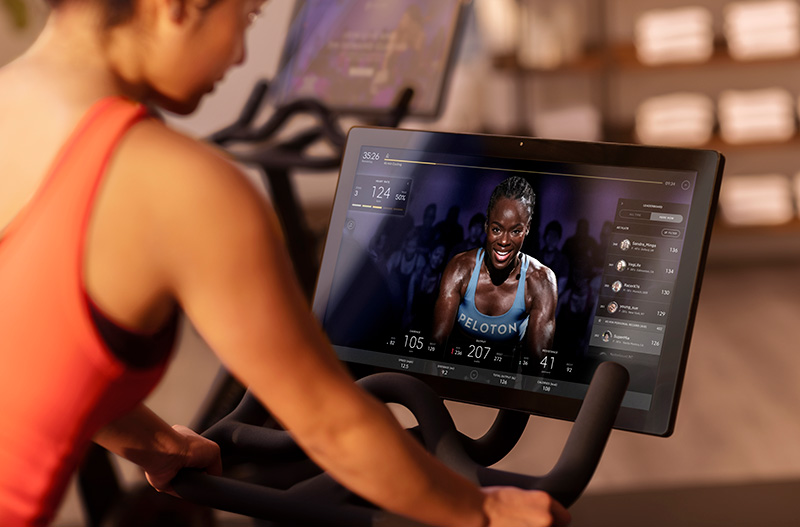 Woman riding a Peloton bike. There is an instructor on the screen guiding her through the exercise.